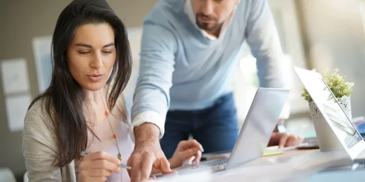 Mujer sonriente y hombre concentrado trabajando en equipo para optimizar la velocidad de carga y SEO de un sitio web peruano.