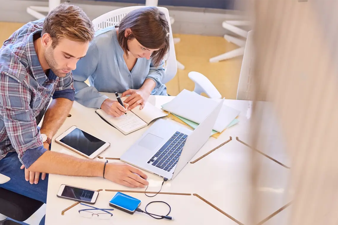 Mejores prácticas para enlaces internos La supervisora, mirando la laptop del marketer y tomando apuntes sobre las mejores prácticas para la utilización efectiva de enlaces internos.