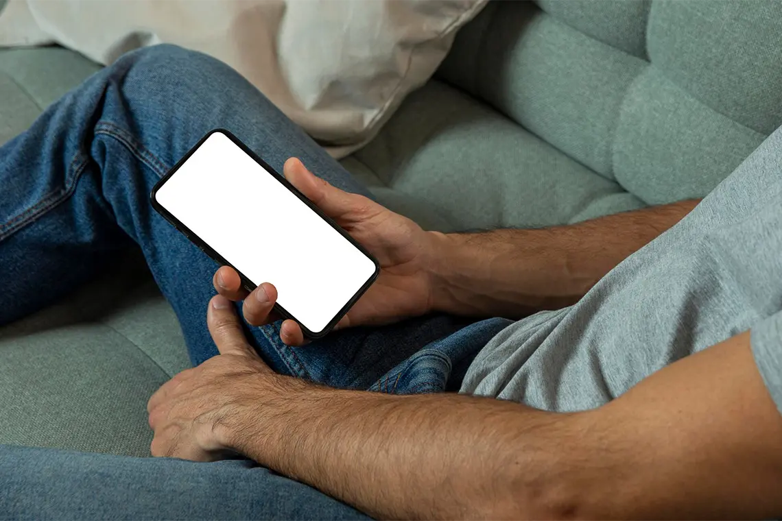 Importancia de las Palabras Clave en el SEO El hombre, ahora recostado en el sofá verde, analiza los resultados de una búsqueda de palabras clave realizada con una herramienta especializada en su movil.