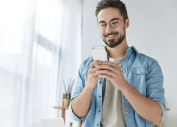 Joven sonriente revisando con alegría las notificaciones en su celular. Estructura de URL eficiente