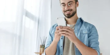 Joven sonriente revisando con alegría las notificaciones en su celular. Estructura de URL eficiente