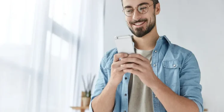 Joven sonriente revisando con alegría las notificaciones en su celular. Estructura de URL eficiente