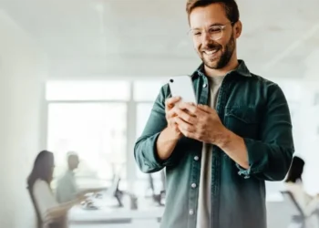 Hombre sonriente revisando su celular, rodeado de personas en un ambiente local. Contenido para Plataformas Locales en Perú.