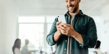 Hombre sonriente revisando su celular, rodeado de personas en un ambiente local. Contenido para Plataformas Locales en Perú.