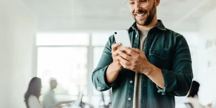 Hombre sonriente revisando su celular, rodeado de personas en un ambiente local. Contenido para Plataformas Locales en Perú.