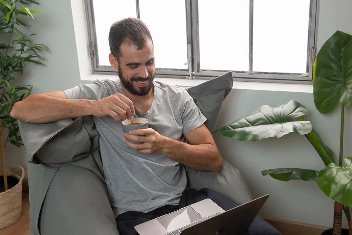 Análisis de Competencia de Palabras Clave El hombre, sonriendo mientras observa la pantalla de su laptop, analiza las estrategias utilizadas por sus competidores con herramientas para investigar palabras clave.