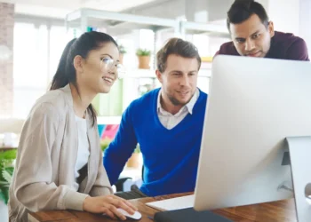 Un equipo de marketing, compuesto por dos hombres y una mujer, analiza una página web en una PC, con la mujer señalando un elemento. [Impacto de metaetiquetas en SEO]