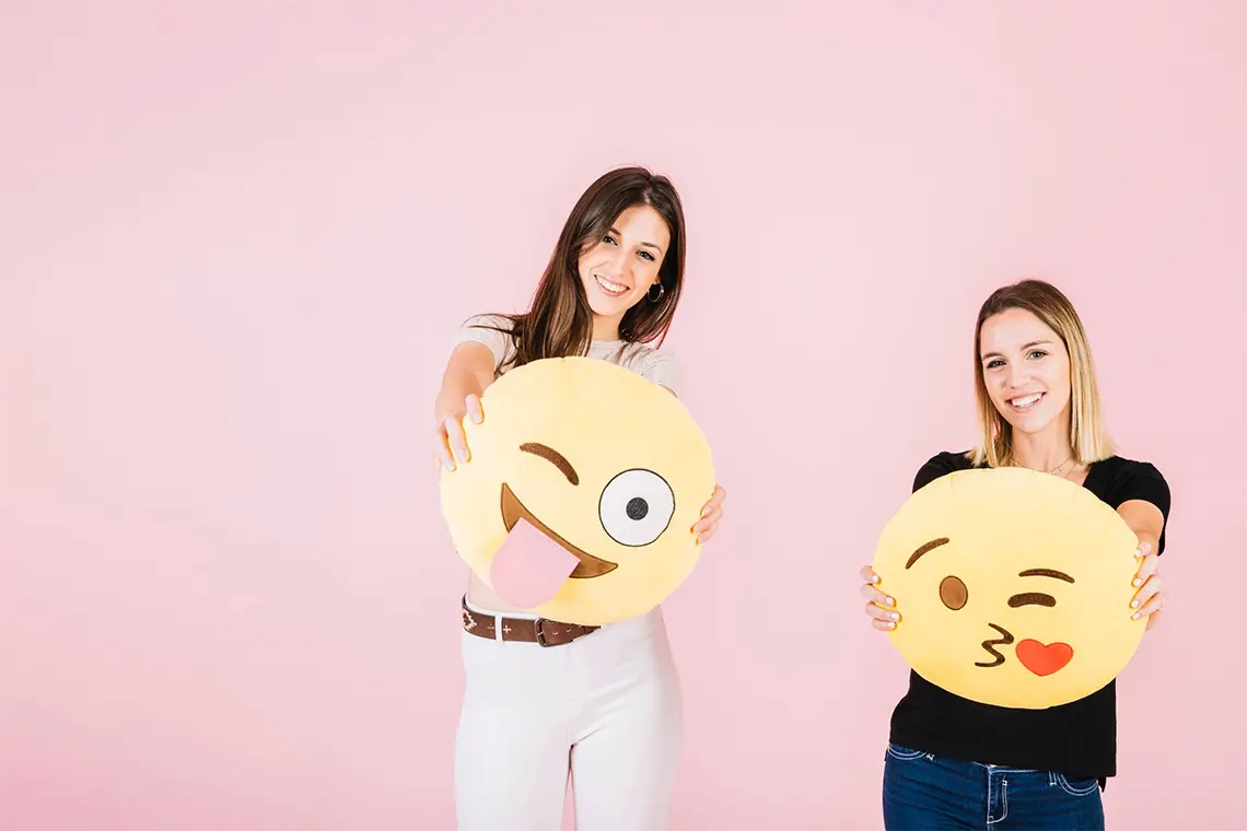 Dos jóvenes sonrientes, ambas con almohadas de emoji de caras amarillas, simbolizando el futuro del CTR local en Arequipa con la integración de emojis SEO.