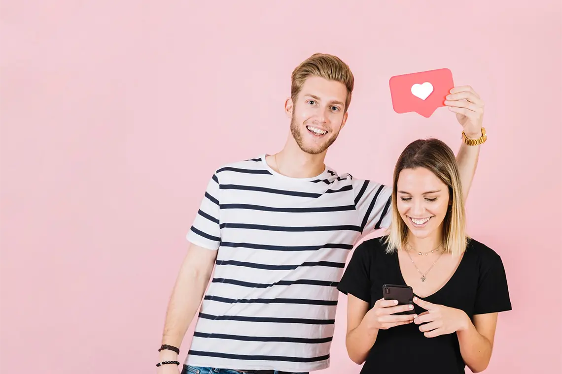 Dos jóvenes, uno con un cartel de “corazón” y la otra con una sonrisa viendo su celular, analizan el impacto de los emojis en el CTR orgánico y su influencia en el posicionamiento SEO local en Arequipa.