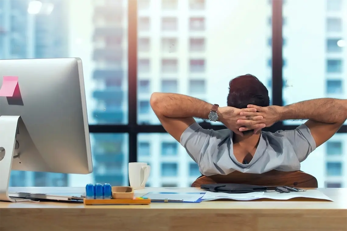 El joven profesional, con las manos en la nuca, observa las oficinas y edificios de su alrededor, buscando inspiración para sus estrategias de marketing.