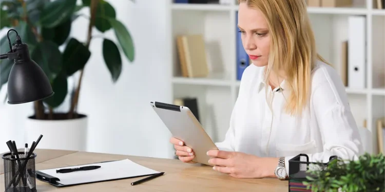 Una mujer, sentada en una oficina, observa con atención los datos de su tablet relacionados con el análisis de competencia en marketing digital.