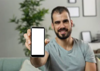 Un hombre sonriente, sentado en un sofá verde, sostiene su celular mostrando la aplicación de herramientas para investigar palabras clave.