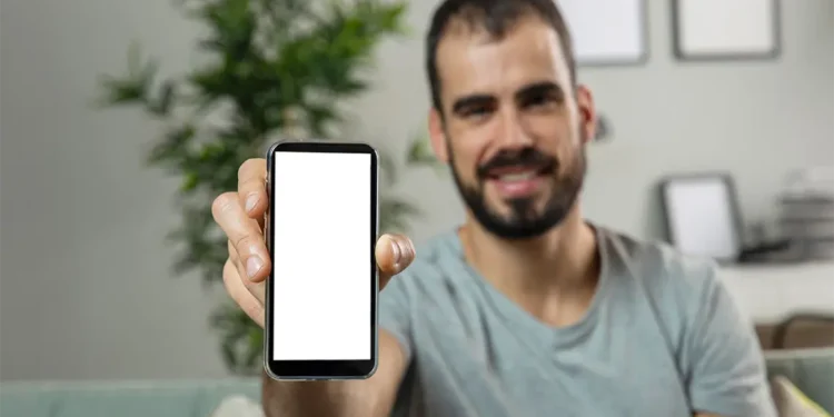 Un hombre sonriente, sentado en un sofá verde, sostiene su celular mostrando la aplicación de herramientas para investigar palabras clave.