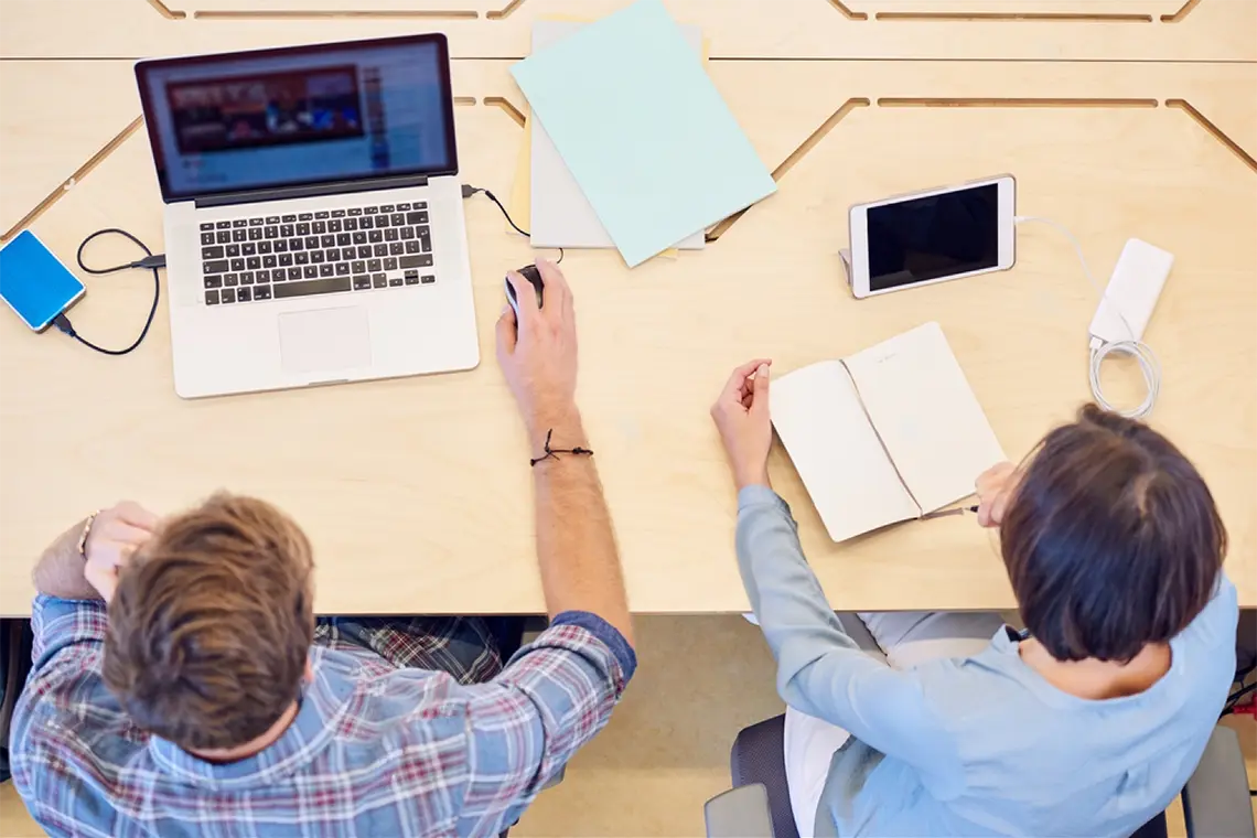 ¿Qué son los enlaces internos? Una toma desde arriba del trabajo del marketer en su laptop y la supervisora tomando apuntes sobre la estrategia de enlaces internos.