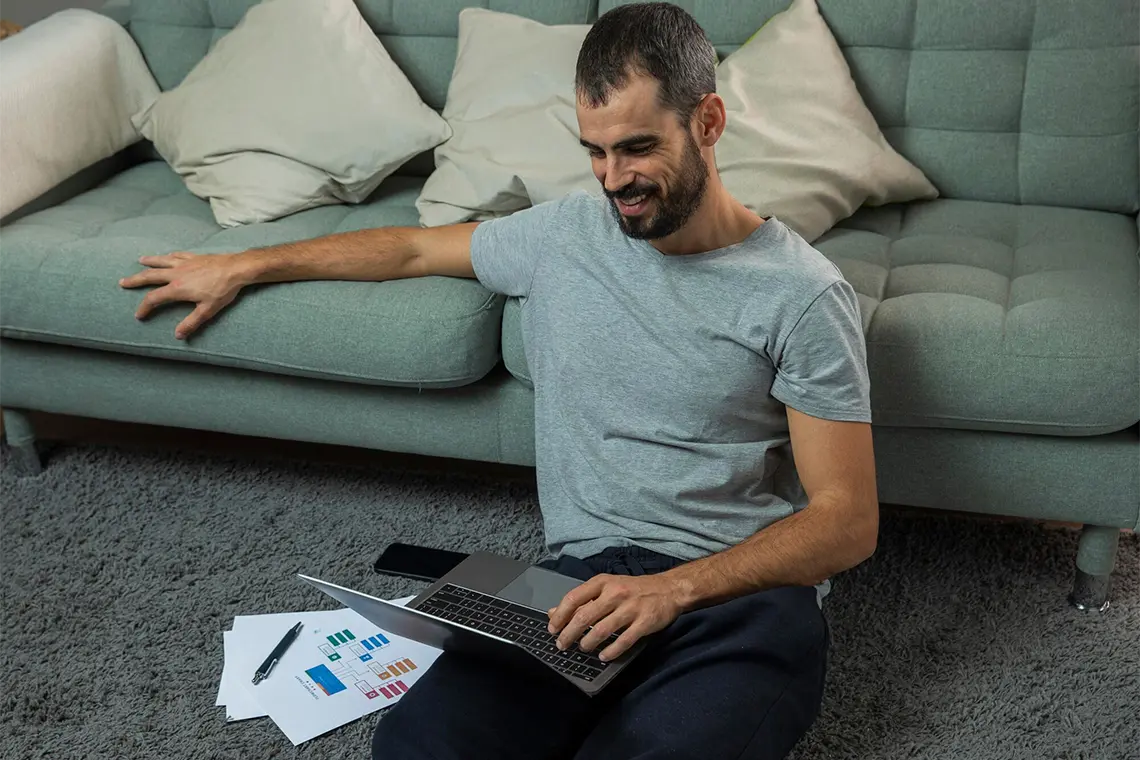 Optimización de Palabras Clave El hombre, ahora en el suelo con su laptop como apoyo, trabaja en la optimización de las palabras clave en el contenido de su sitio web.