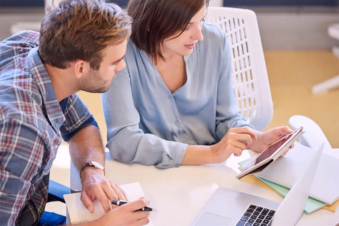 Mejorar la estructura de navegación con enlaces internos El marketer, tomando apuntes de lo que la supervisora le está mostrando en la tablet sobre cómo mejorar la estructura de navegación y la utilización efectiva de enlaces internos.