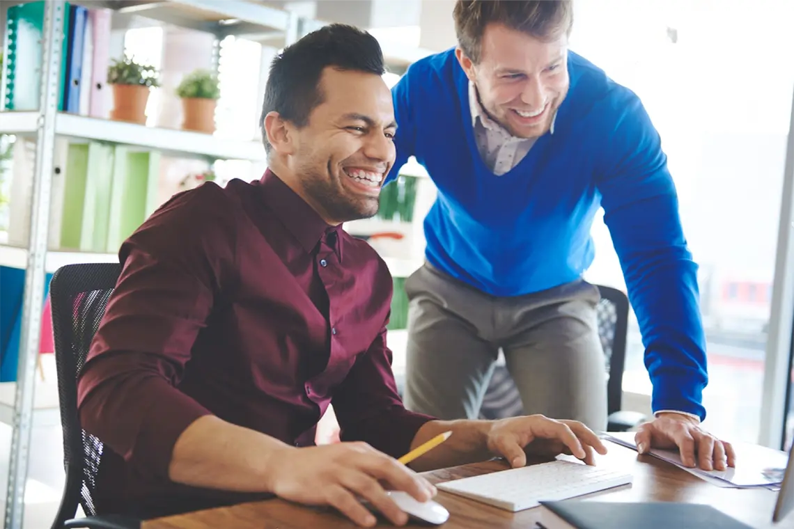 Los dos hombres sonríen mientras observan los resultados de la optimización de las metaetiquetas en una PC. [Impacto de metaetiquetas en SEO]